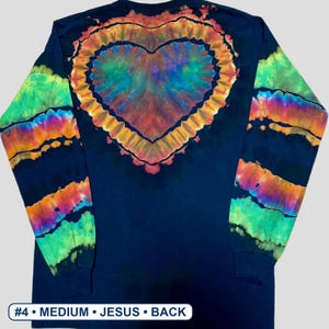May include: A long-sleeve navy blue shirt featuring a large, central tie-dye heart pattern in shades of orange, yellow, green, and purple. The sleeves display horizontal tie-dye stripes in matching vibrant colours. Text at the bottom reads #4 &bull; MEDIUM &bull; JESUS &bull; BACK.
