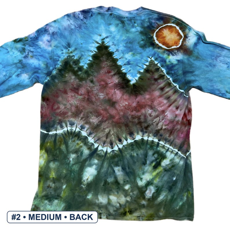 May include: A long-sleeve tie-dye shirt featuring a landscape design with a blue sky, a bright orange sun, and dark green mountain silhouettes. The shirt displays a horizontal white line separating the mountains from the forest floor.