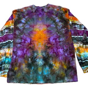May include: A long-sleeve shirt featuring a tie-dye pattern with a vibrant central burst of orange surrounded by deep purple, black, and blue hues. The sleeves display horizontal bands of orange, purple, black, and turquoise colors.