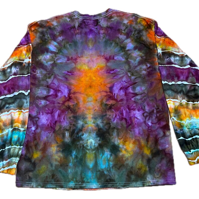 May include: A long-sleeve shirt featuring a tie-dye pattern with a vibrant central burst of orange surrounded by deep purple, black, and blue hues. The sleeves display horizontal bands of orange, purple, black, and turquoise colors.