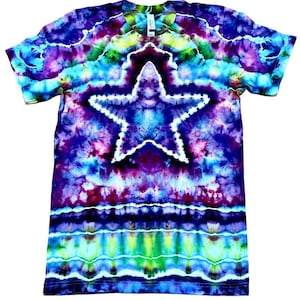 May include: A tie-dye t-shirt with a large white star design in the center. The shirt features a vibrant mix of colors, including blue, purple, green, and yellow. The shirt is short-sleeved and has a crew neck.
