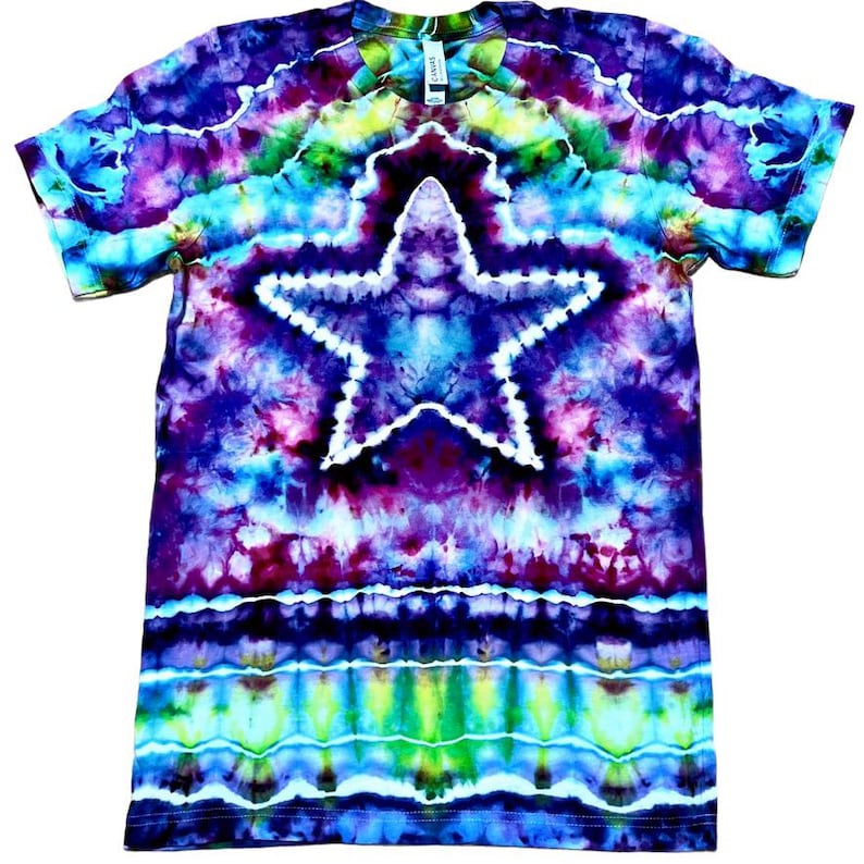May include: A tie-dye t-shirt with a large white star design in the center. The shirt features a vibrant mix of colors, including blue, purple, green, and yellow. The shirt is short-sleeved and has a crew neck.