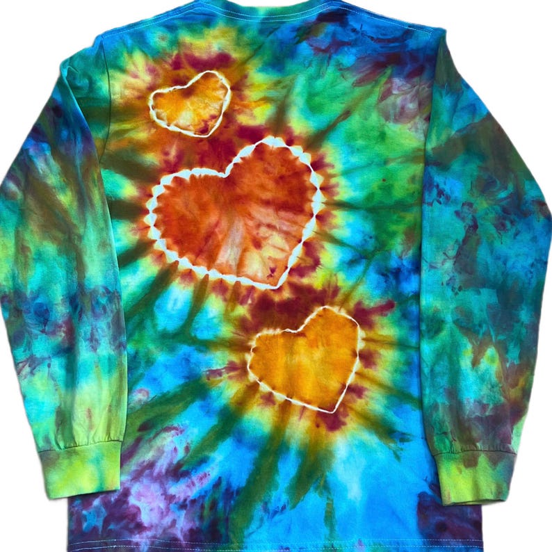 Może przedstawiać: Koszulka z długim rękawem z żywym wzorem tie-dye w odcieniach niebieskiego, zielonego, ż&oacute;łtego i fioletowego. Wz&oacute;r zawiera trzy wyraźne motywy w kształcie serca w kolorze pomarańczowym i ż&oacute;łtym, każdy z białą obw&oacute;dką na tle.