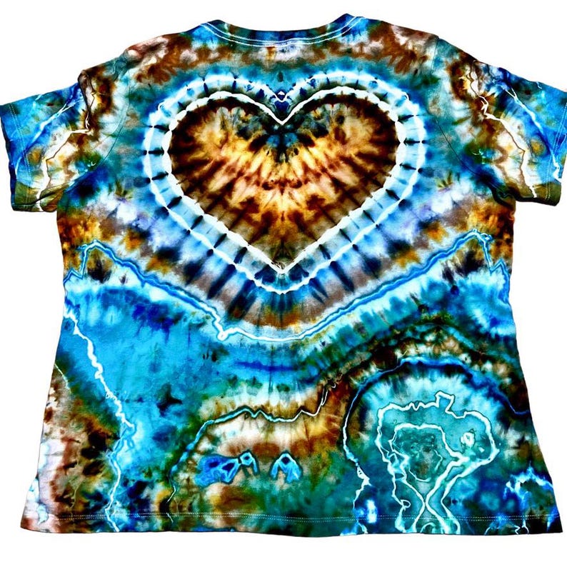 May include: A short-sleeve t-shirt featuring a tie-dye pattern in shades of turquoise, deep blue, brown, and white. The design showcases a prominent central heart shape outlined in white, surrounded by swirling, geode-like organic patterns.