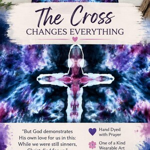 May include: A long-sleeve shirt featuring a tie-dye pattern in shades of purple, blue, and black with a white cross design. The text reads: The Cross CHANGES EVERYTHING, Romans 5:8, Hand Dyed with Prayer, One of a Kind Wearable Art, Made to Inspire Faith Every Day, and Colors of Grace Designs.