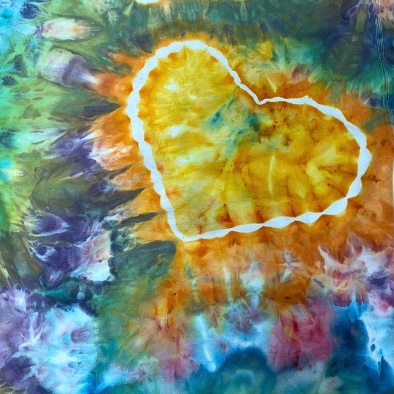 May include: A tie-dye fabric featuring a prominent central heart shape outlined in white. The heart is filled with vibrant shades of yellow and orange, while the surrounding area displays a swirling pattern of green, blue, purple, and pink hues.
