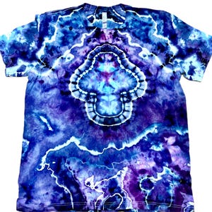 以下が含まれることがあります： 青、紫、白の色合いのタイダイTシャツ。シャツの中央には、様式化されたキノコまたは花に似たデザインがあります。パターンは対称的で、渦巻く有機的な美しさがあります。シャツは半袖で、クルーネックです。