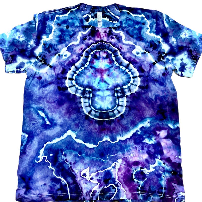 以下が含まれることがあります： 青、紫、白の色合いのタイダイTシャツ。シャツの中央には、様式化されたキノコまたは花に似たデザインがあります。パターンは対称的で、渦巻く有機的な美しさがあります。シャツは半袖で、クルーネックです。