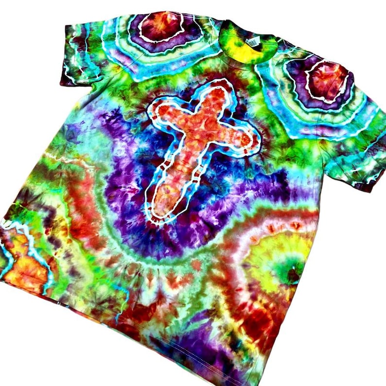 Może przedstawiać: Koszulka tie-dye z motywem krzyża. Koszulka prezentuje żywą mieszankę kolor&oacute;w, w tym czerwony, pomarańczowy, ż&oacute;łty, zielony, niebieski i fioletowy, tworząc efekt psychodeliczny. Krzyż jest obrysowany na biało.