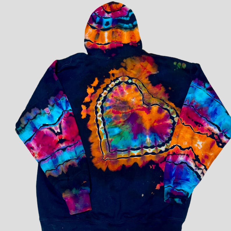May include: A black hooded sweatshirt featuring a vibrant tie-dye heart design on the back. The heart is composed of bright orange, pink, blue, and green colors. The sleeves and hood also display matching tie-dye patterns in the same colors.