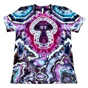 Puede incluir: Una camiseta de manga corta con un complejo patr&oacute;n de te&ntilde;ido anudado en tonos p&uacute;rpura intenso, magenta, negro y cian brillante. El dise&ntilde;o muestra formas circulares conc&eacute;ntricas similares a geodas con contornos blancos sobre la tela.