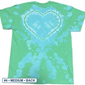 Peut inclure: Un t-shirt &agrave; manches courtes avec un motif tie-dye dans des tons vert clair et turquoise vif. Le centre du t-shirt pr&eacute;sente une forme de c&oelig;ur pro&eacute;minente cr&eacute;&eacute;e par le processus de teinture. Une &eacute;tiquette en bas indique #4 &bull; MEDIUM &bull; BACK.