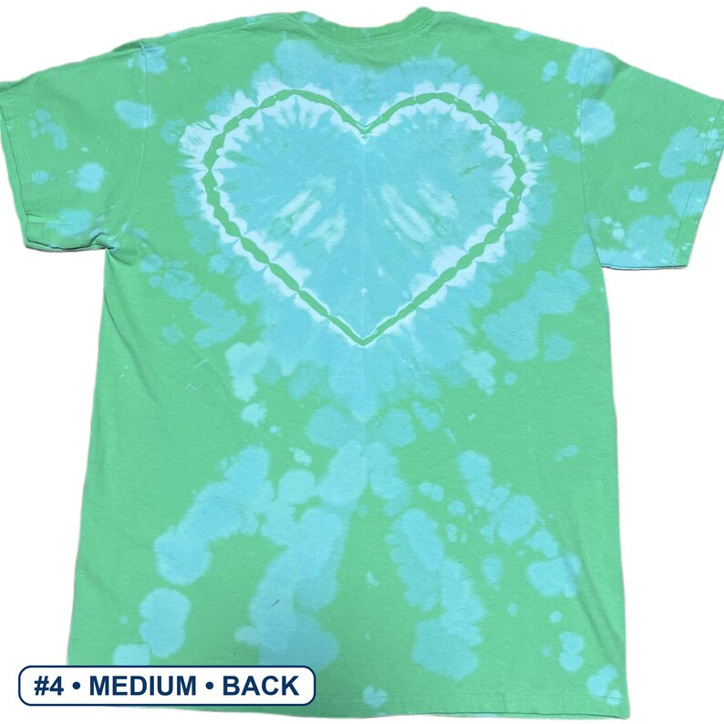 Peut inclure: Un t-shirt &agrave; manches courtes avec un motif tie-dye dans des tons vert clair et turquoise vif. Le centre du t-shirt pr&eacute;sente une forme de c&oelig;ur pro&eacute;minente cr&eacute;&eacute;e par le processus de teinture. Une &eacute;tiquette en bas indique #4 &bull; MEDIUM &bull; BACK.