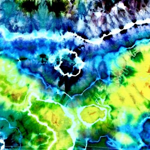 Op de afbeelding: Abstract tie-dye patroon in tinten blauw, groen en geel. Het ontwerp heeft wervelende patronen en een aquareleffect, met een mix van donkere en lichte tinten. De stof lijkt een zacht materiaal te zijn.