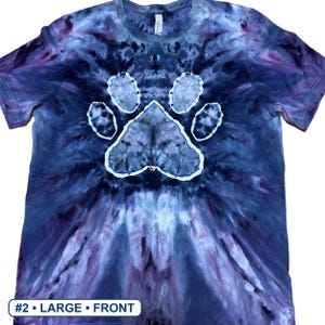Może przedstawiać: Koszulka z kr&oacute;tkim rękawem i okrągłym dekoltem z wzorem tie-dye w odcieniach ciemnego błękitu, fioletu i czerni. Na środku koszulki znajduje się wyraźny biały nadruk w kształcie łapy. Tekst #2 &bull; LARGE &bull; FRONT jest widoczny w dolnym rogu.