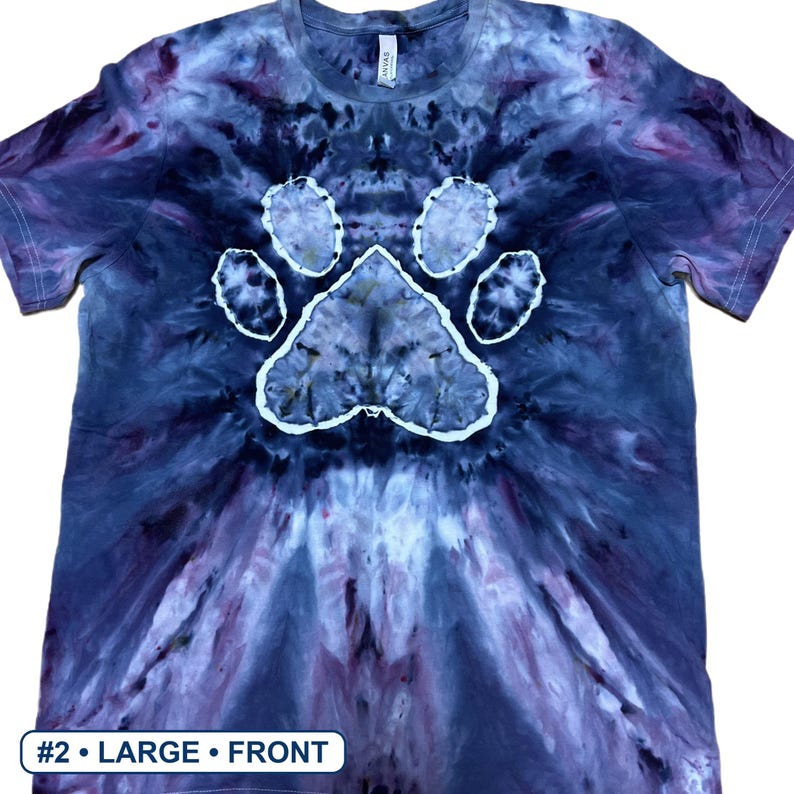 Może przedstawiać: Koszulka z kr&oacute;tkim rękawem i okrągłym dekoltem z wzorem tie-dye w odcieniach ciemnego błękitu, fioletu i czerni. Na środku koszulki znajduje się wyraźny biały nadruk w kształcie łapy. Tekst #2 &bull; LARGE &bull; FRONT jest widoczny w dolnym rogu.