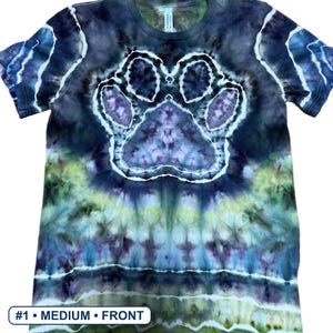 Może przedstawiać: Koszulka z kr&oacute;tkim rękawem z wzorem tie-dye w odcieniach ciemnego błękitu, fioletu i limonki. Na środku koszulki znajduje się wyraźny wz&oacute;r odcisku łapy z białym obrysem, z widocznym tekstem #1 &bull; MEDIUM &bull; FRONT na dole obrazu.