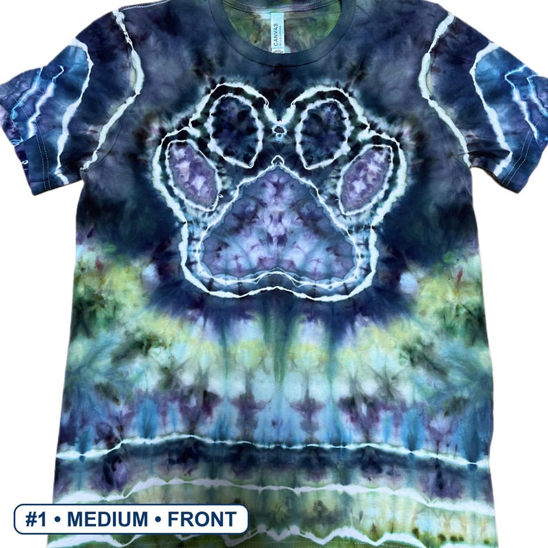 Może przedstawiać: Koszulka z kr&oacute;tkim rękawem z wzorem tie-dye w odcieniach ciemnego błękitu, fioletu i limonki. Na środku koszulki znajduje się wyraźny wz&oacute;r odcisku łapy z białym obrysem, z widocznym tekstem #1 &bull; MEDIUM &bull; FRONT na dole obrazu.