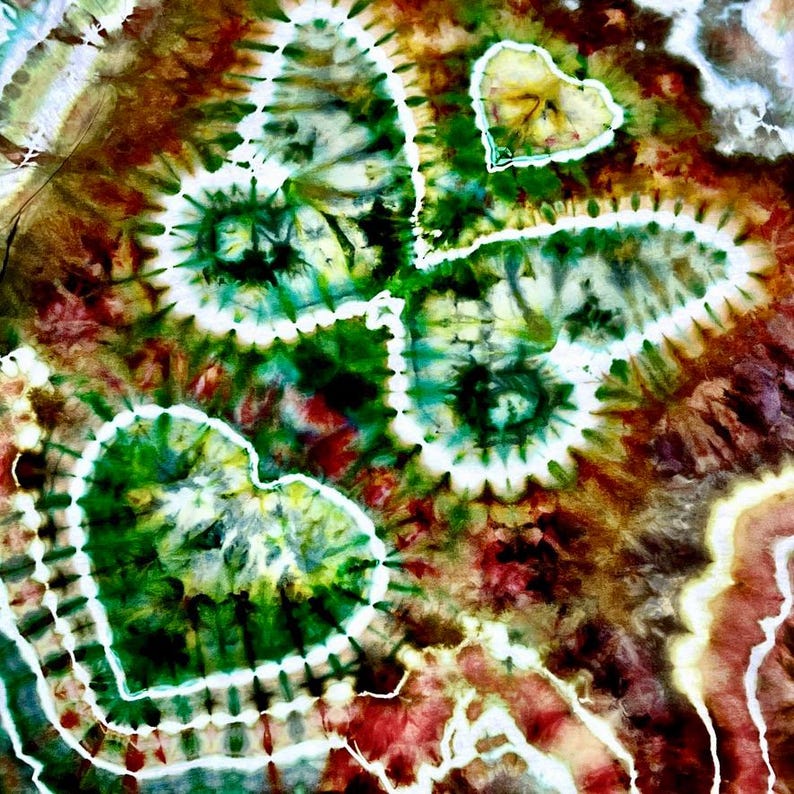 May include: Abstract tie-dye textile with a heart-shaped design. The fabric features a vibrant mix of colors, including green, brown, red, and white. The heart shapes are outlined in white, creating a striking contrast against the colorful background.