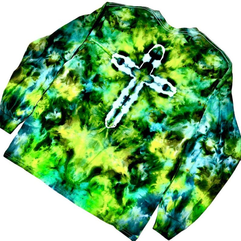 May include: A long-sleeve shirt featuring a tie-dye pattern in shades of lime green, forest green, and dark blue. The center of the shirt displays a prominent white cross shape created by the tie-dye technique, with long sleeves and a crew neckline.