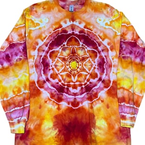 Puede incluir: Una camiseta de manga larga con cuello redondo que presenta un vibrante patr&oacute;n tie-dye en tonos naranja, amarillo y magenta intenso. El centro de la prenda muestra un dise&ntilde;o circular sim&eacute;trico con l&iacute;neas blancas que irradian.