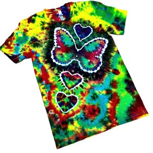 May include: A tie-dye t-shirt with a butterfly and heart design. The shirt features a vibrant mix of colors, including yellow, green, red, and blue. The butterfly and hearts are outlined in white, creating a striking contrast against the colorful background.