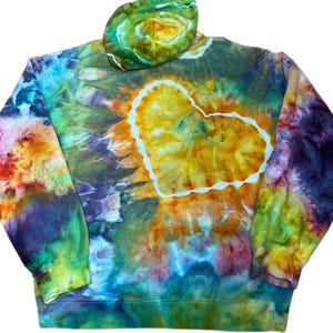 May include: A long-sleeve hooded sweatshirt featuring a vibrant tie-dye pattern in shades of yellow, orange, green, blue, and purple. A large, central heart shape is outlined in white, with a matching tie-dye pattern on the attached hood.