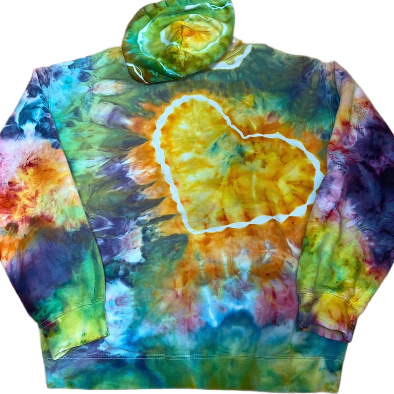 May include: A long-sleeve hooded sweatshirt featuring a vibrant tie-dye pattern in shades of yellow, orange, green, blue, and purple. A large, central heart shape is outlined in white, with a matching tie-dye pattern on the attached hood.