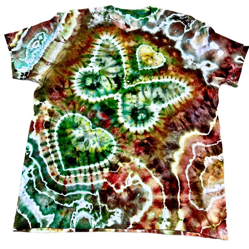 May include: A tie-dye t-shirt with a butterfly and heart design. The shirt features a vibrant mix of colors, including green, brown, red, and white. The butterfly and heart shapes are prominent, with a spiral pattern in the center of the butterfly.
