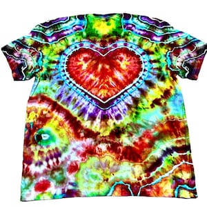 Może przedstawiać: Koszulka typu tie-dye z dużym sercem pośrodku. Koszulka ma żywą mieszankę kolor&oacute;w, w tym czerwony, ż&oacute;łty, zielony, niebieski i fioletowy. Serce jest obrysowane na biało, a wz&oacute;r tie-dye promieniuje na zewnątrz.