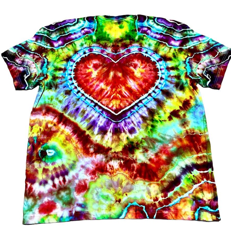 Może przedstawiać: Koszulka typu tie-dye z dużym sercem pośrodku. Koszulka ma żywą mieszankę kolor&oacute;w, w tym czerwony, ż&oacute;łty, zielony, niebieski i fioletowy. Serce jest obrysowane na biało, a wz&oacute;r tie-dye promieniuje na zewnątrz.