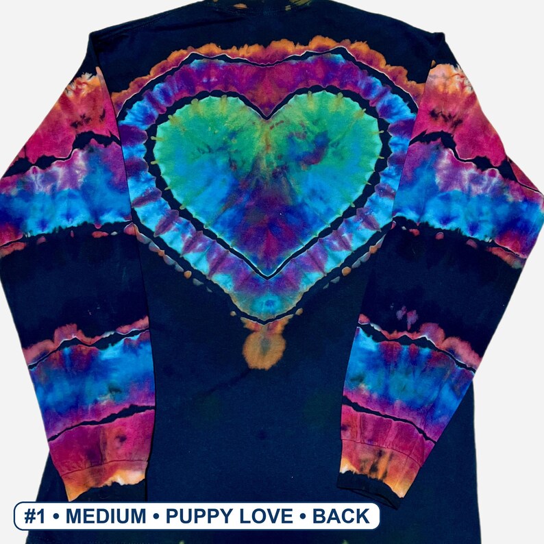 May include: A long-sleeve shirt with a black base featuring a tie-dye heart design in shades of blue, green, purple, and orange. The sleeves have horizontal tie-dye stripes. Text at the bottom reads #1 &bull; MEDIUM &bull; PUPPY LOVE &bull; BACK.