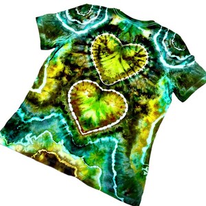 Puede incluir: Una camiseta te&ntilde;ida con tinte en tonos verdes, amarillos y azules. Dos grandes formas de coraz&oacute;n est&aacute;n delineadas en blanco en la parte posterior de la camiseta. La camiseta tiene mangas cortas y cuello redondo.