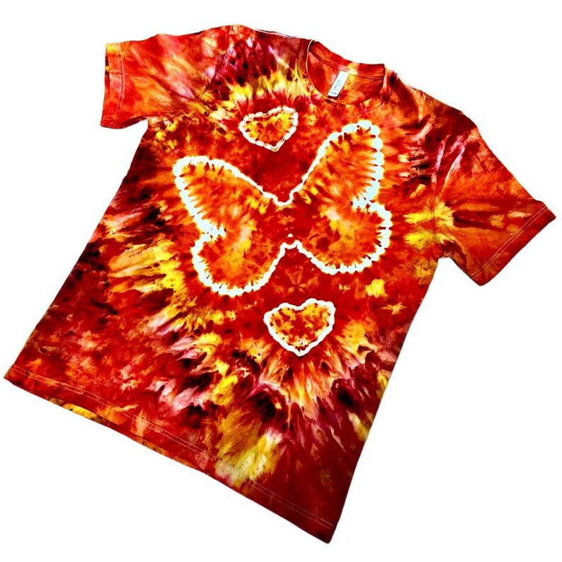 May include: A tie-dye t-shirt in shades of red, orange, and yellow. The shirt features a large butterfly design and two heart shapes outlined in white. The shirt is a short-sleeved crew neck.