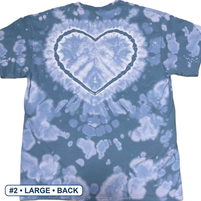 Peut inclure: Un t-shirt &agrave; manches courtes pr&eacute;sentant un motif tie-dye bleu et blanc avec une forme de c&oelig;ur pro&eacute;minente centr&eacute;e au dos. Le tissu affiche un effet nuageux et tachet&eacute; dans des tons bleu ardoise et blanc. Une &eacute;tiquette indique #2 &bull; LARGE &bull; BACK.