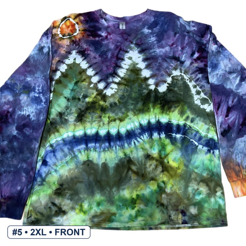 May include: A long-sleeve tie-dye shirt featuring a mountain range pattern in shades of purple, green, blue, and white. The design includes a circular sun motif in the upper left corner and a horizontal band of blue across the centre of the chest.