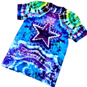 May include: A tie-dye t-shirt with a large star design. The shirt features a vibrant mix of colors, including blues, purples, and greens. The star is outlined in white, creating a striking contrast against the colorful background. The shirt is a short-sleeved crew neck.