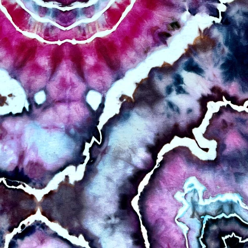 Puede incluir: Un tejido con un patr&oacute;n de te&ntilde;ido anudado en tonos vibrantes de magenta, morado intenso y azul oscuro. El dise&ntilde;o muestra formas org&aacute;nicas y arremolinadas separadas por l&iacute;neas blancas dentadas que crean un efecto de geoda de alto contraste.