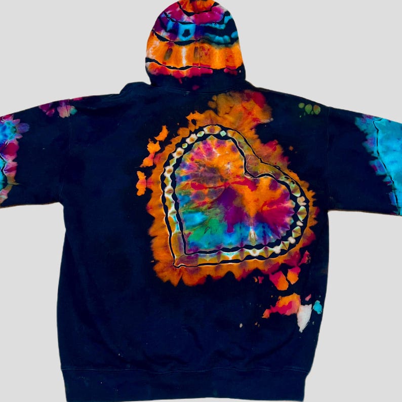 May include: A black hooded sweatshirt featuring a large, central tie-dye heart design in vibrant shades of orange, purple, blue, and pink. The heart is outlined with a decorative pattern, and the hood also displays a matching tie-dye pattern.