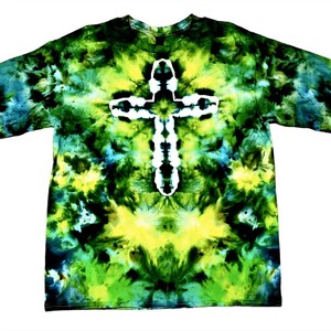 May include: A short-sleeve t-shirt featuring a tie-dye pattern in shades of forest green, lime green, black, and teal. The center of the shirt displays a prominent white cross shape created through the tie-dye process against the dark background.