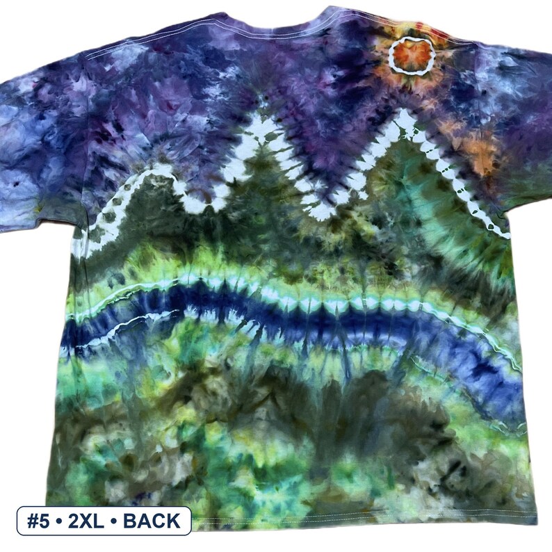 May include: A short-sleeve t-shirt featuring a tie-dye pattern with a mountain landscape design in shades of purple, dark green, lime green, and blue. A white sun-like circle is at the top right. Text at the bottom left reads #5 &bull; 2XL &bull; BACK.