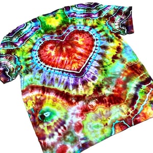 Może przedstawiać: Koszulka typu tie-dye z dużym sercem pośrodku. Serce jest czerwone z białym konturem, otoczone niebieskim pierścieniem. Koszulka ma żywą mieszankę kolor&oacute;w, w tym ż&oacute;łty, zielony, fioletowy i czerwony, tworząc efekt psychodeliczny.