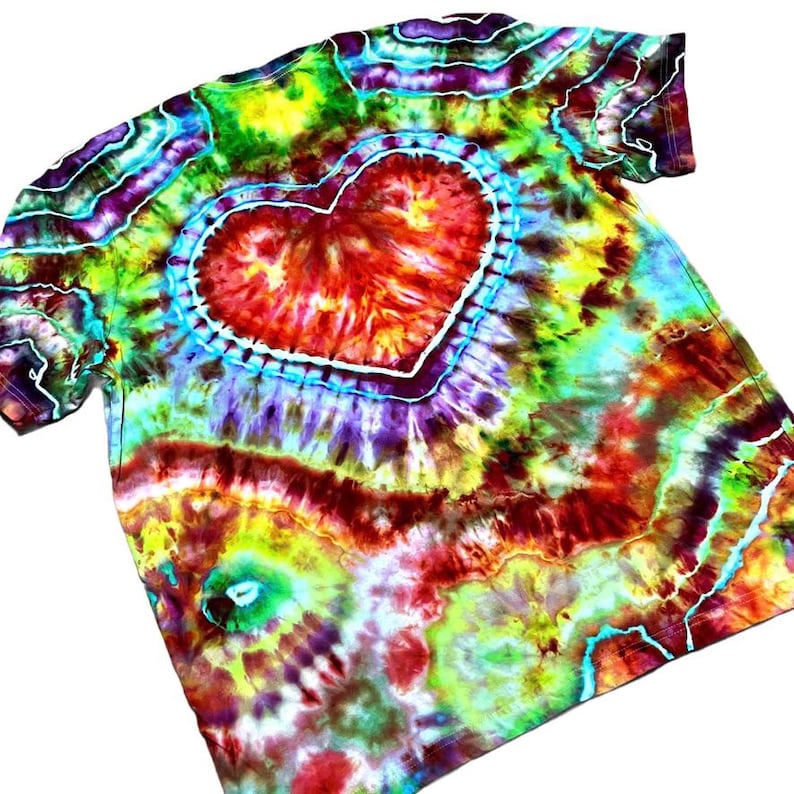 Może przedstawiać: Koszulka typu tie-dye z dużym sercem pośrodku. Serce jest czerwone z białym konturem, otoczone niebieskim pierścieniem. Koszulka ma żywą mieszankę kolor&oacute;w, w tym ż&oacute;łty, zielony, fioletowy i czerwony, tworząc efekt psychodeliczny.