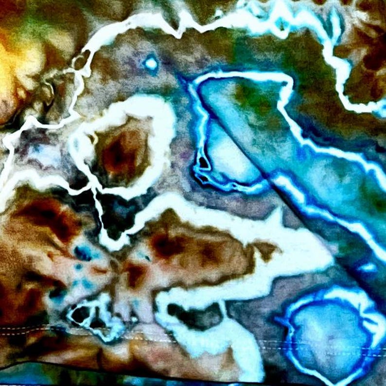 May include: A fabric surface featuring a tie-dye pattern with swirling organic shapes in shades of brown, dark green, and deep blue. Bright white, glowing lines trace the contours of the shapes, creating a high-contrast effect across the textile.