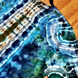 May include: A long-sleeved tie-dye shirt in shades of blue, green, and white. The shirt features a unique pattern with diagonal stripes and swirling designs, creating a vibrant and artistic look. The fabric appears soft and comfortable.