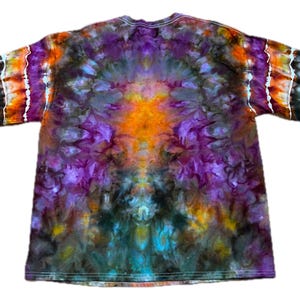 May include: A short-sleeve t-shirt featuring a vibrant tie-dye pattern with a symmetrical design. The colors include deep purple, bright orange, dark charcoal, and hints of teal, blending together in a swirling, organic, and kaleidoscopic effect.