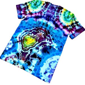 May include: A tie-dye t-shirt with a vibrant, swirling pattern. The shirt features a blend of blues, purples, greens, and yellows, creating a psychedelic effect. The design includes circular and organic shapes, making it a unique piece of apparel.