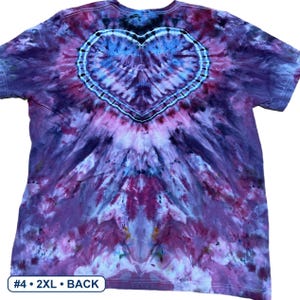 Może przedstawiać: Koszulka z kr&oacute;tkim rękawem z wzorem tie-dye w odcieniach fioletu, r&oacute;żu i błękitu. Wz&oacute;r zawiera wyraźny kształt serca wyśrodkowany na g&oacute;rnej części plec&oacute;w, obrysowany ciemnoniebieską i białą kropkowaną linią. Tekst brzmi #4 2XL BACK.