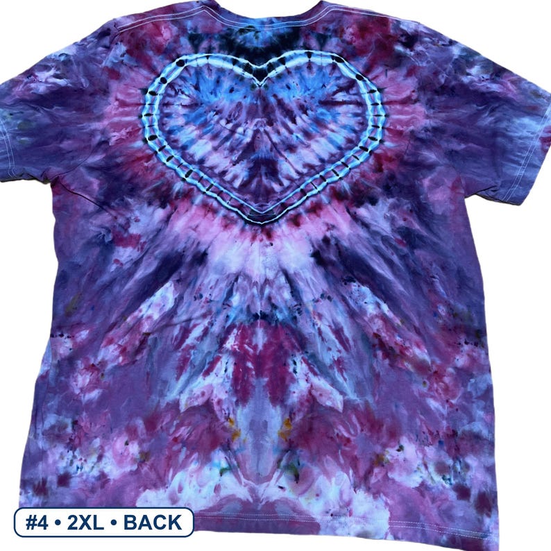 Może przedstawiać: Koszulka z kr&oacute;tkim rękawem z wzorem tie-dye w odcieniach fioletu, r&oacute;żu i błękitu. Wz&oacute;r zawiera wyraźny kształt serca wyśrodkowany na g&oacute;rnej części plec&oacute;w, obrysowany ciemnoniebieską i białą kropkowaną linią. Tekst brzmi #4 2XL BACK.