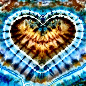 May include: A tie-dye shirt featuring a prominent central heart shape. The design displays a vibrant color palette of deep brown, golden tan, and bright blue, separated by a crisp white outline that defines the heart and radiates outward.